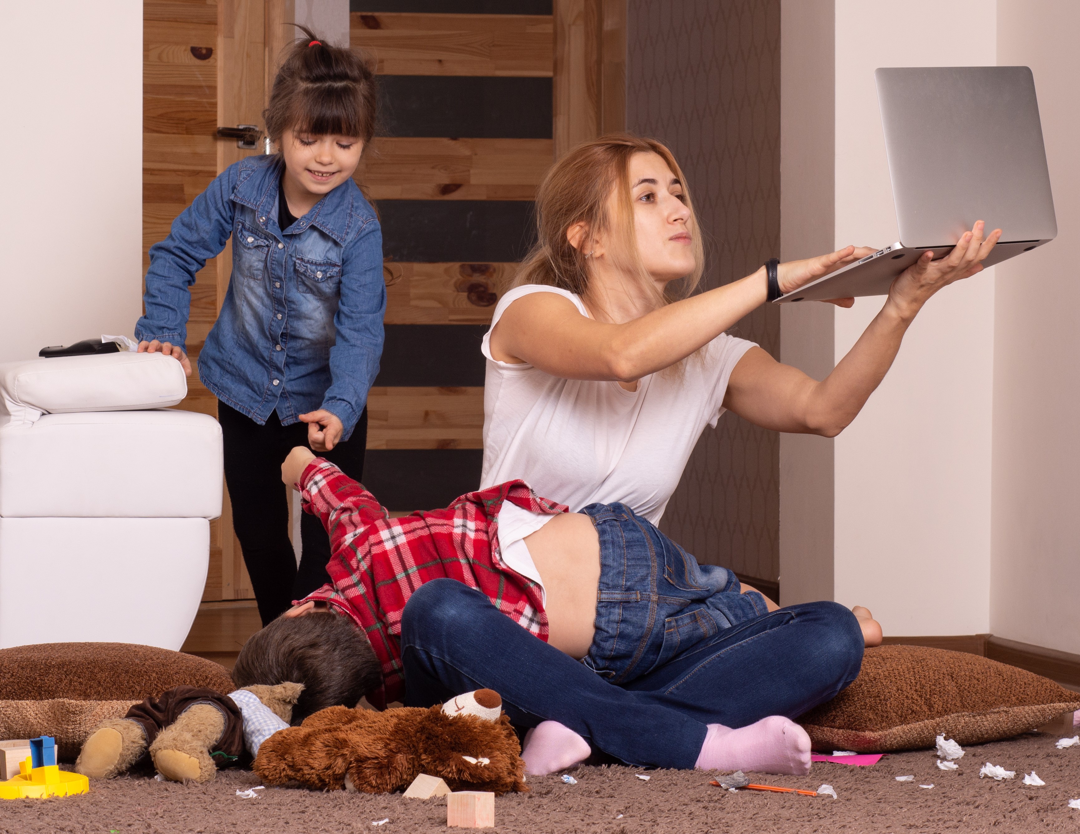 Mom struggling to work on computer while rowdy children climb on her