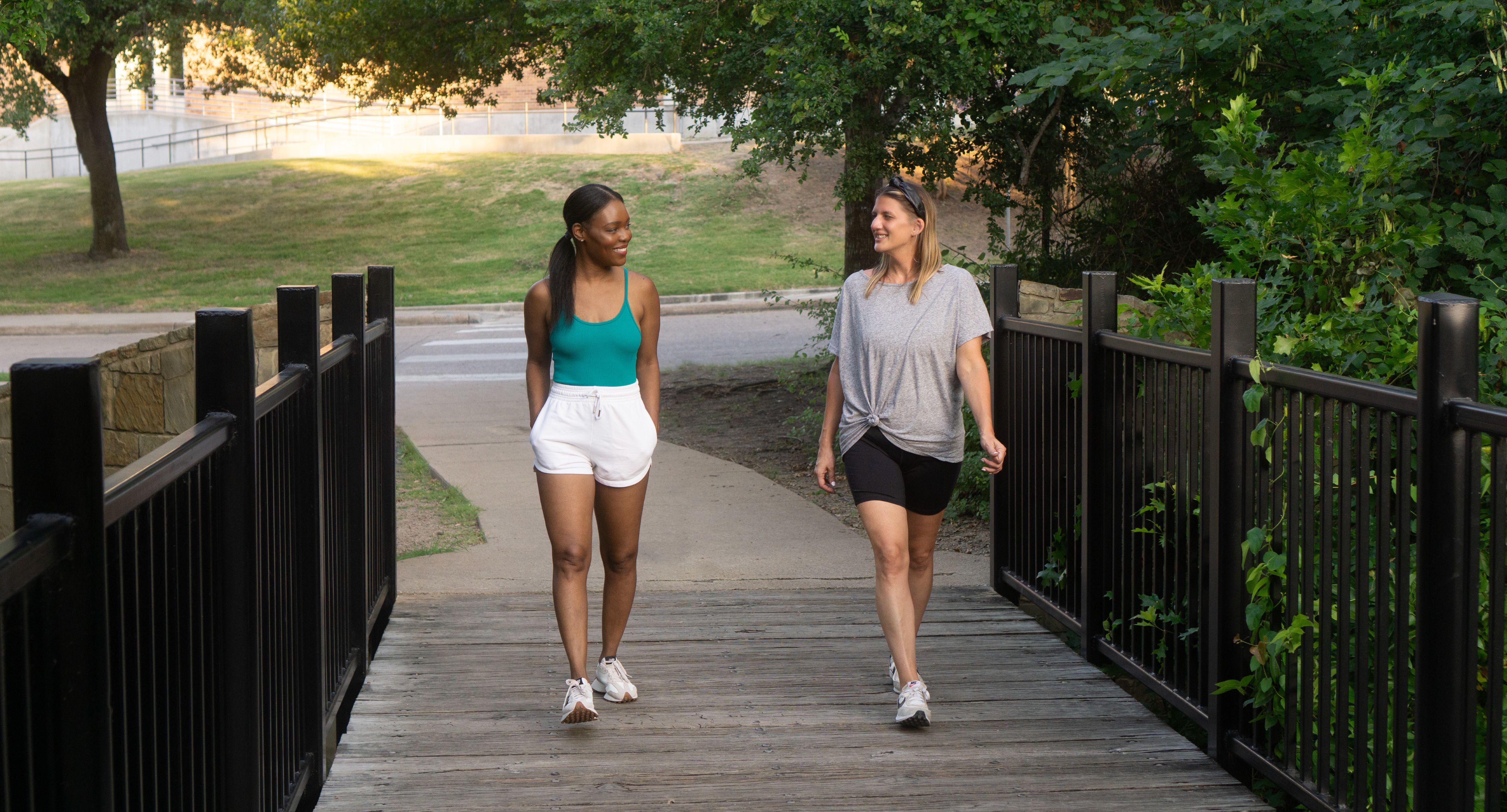Young black woman and whte woman wlak and talk together on college campus